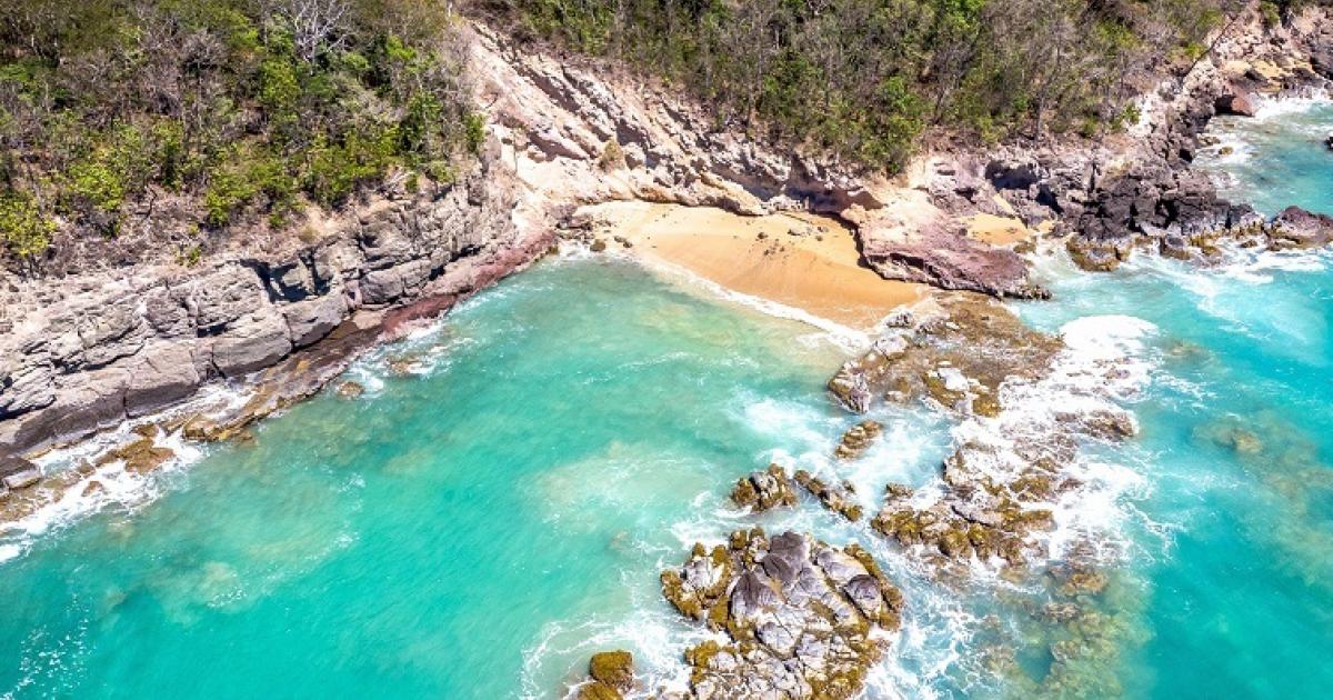 Sable roux, reflets roses et eau émeraude, la crique de la Perle regorge de couleurs